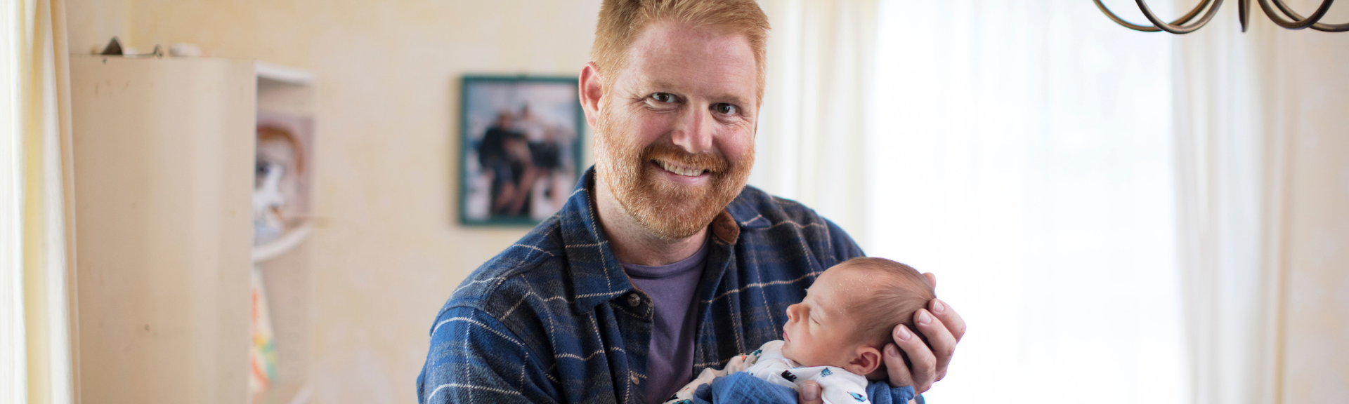 man standing in nursery holding baby and smiling